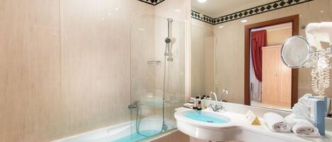 Un baño moderno con ducha de vidrio, lavamanos blanco con recipiente azul y espejo con toallero.