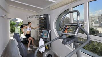 Una palestra con tapis roulant, attrezzature per esercizi e un'ampia vetrata che si affaccia su edifici e alberi.