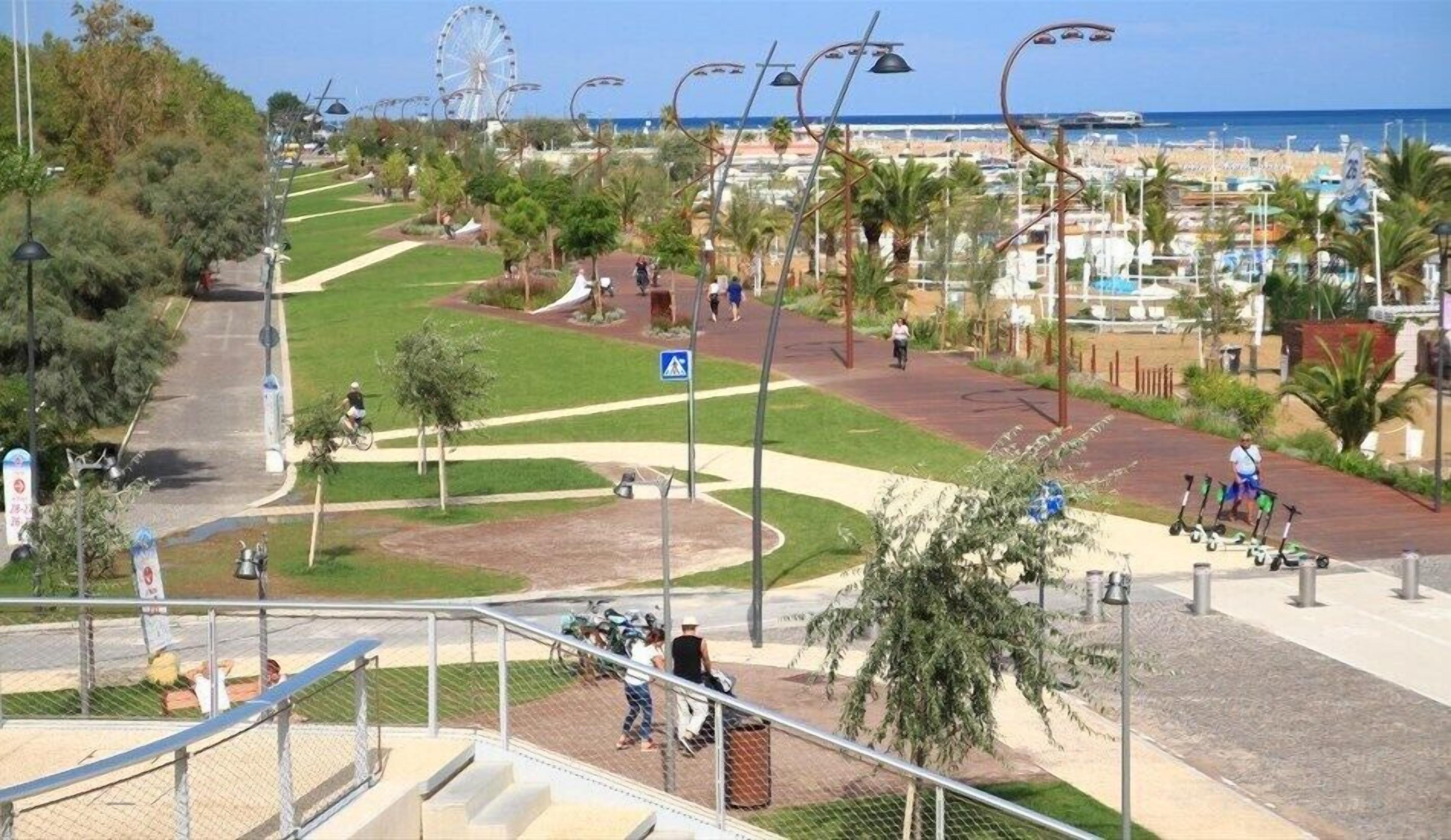 A coastal promenade with a Ferris wheel, palm trees, and a beach in the background.