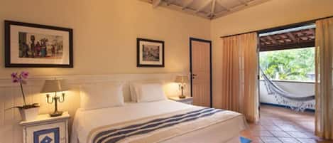 Un dormitorio con una cama grande, una mesita de noche con lámpara, dos cuadros en la pared y vistas al exterior a través de una puerta.