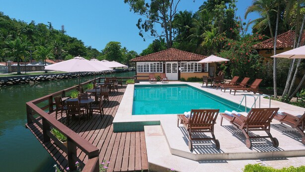 A pool area with wooden deck, lounge chairs, and umbrellas. - Pousada Corsário Paraty (Paraty)