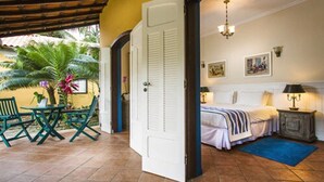 A room with a bed, a nightstand, a table with chairs, and a door leading to another room. - Pousada Corsário Paraty (Paraty)
