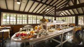 A buffet setup with various food items and beverages, a ceiling fan, and large windows allowing natural light. - Pousada Corsário Paraty (Paraty)