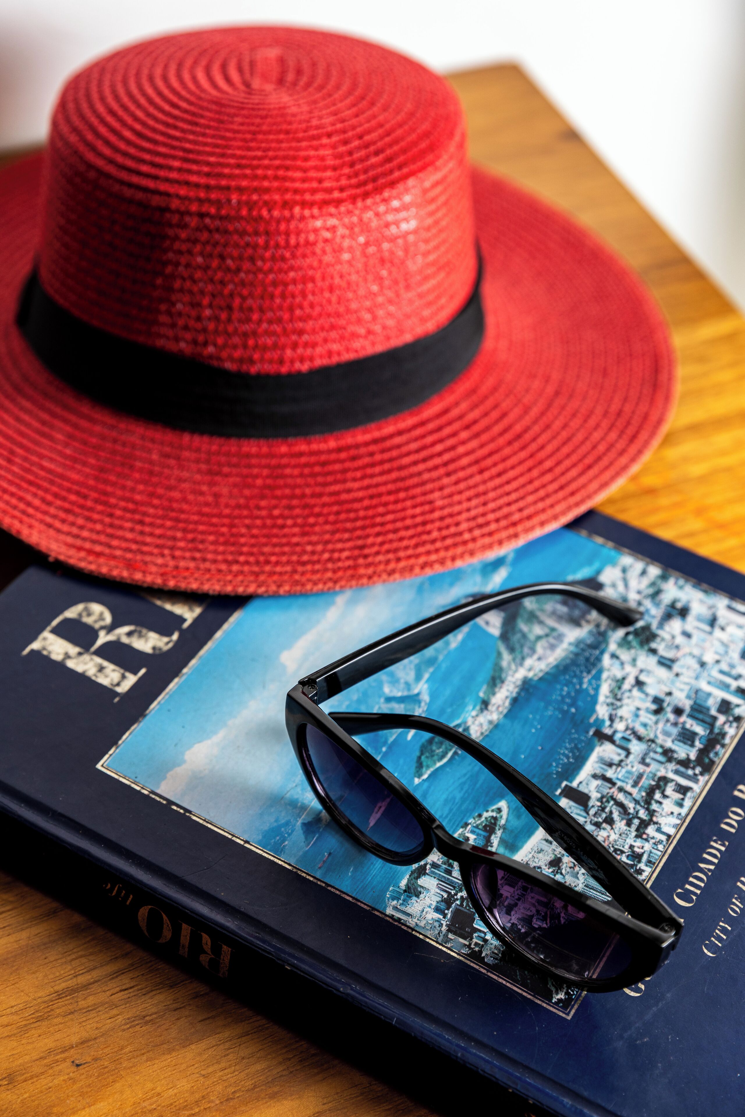 Un sombrero rojo, un par de gafas de sol y un libro con una imagen de un paisaje urbano sobre una superficie de madera.