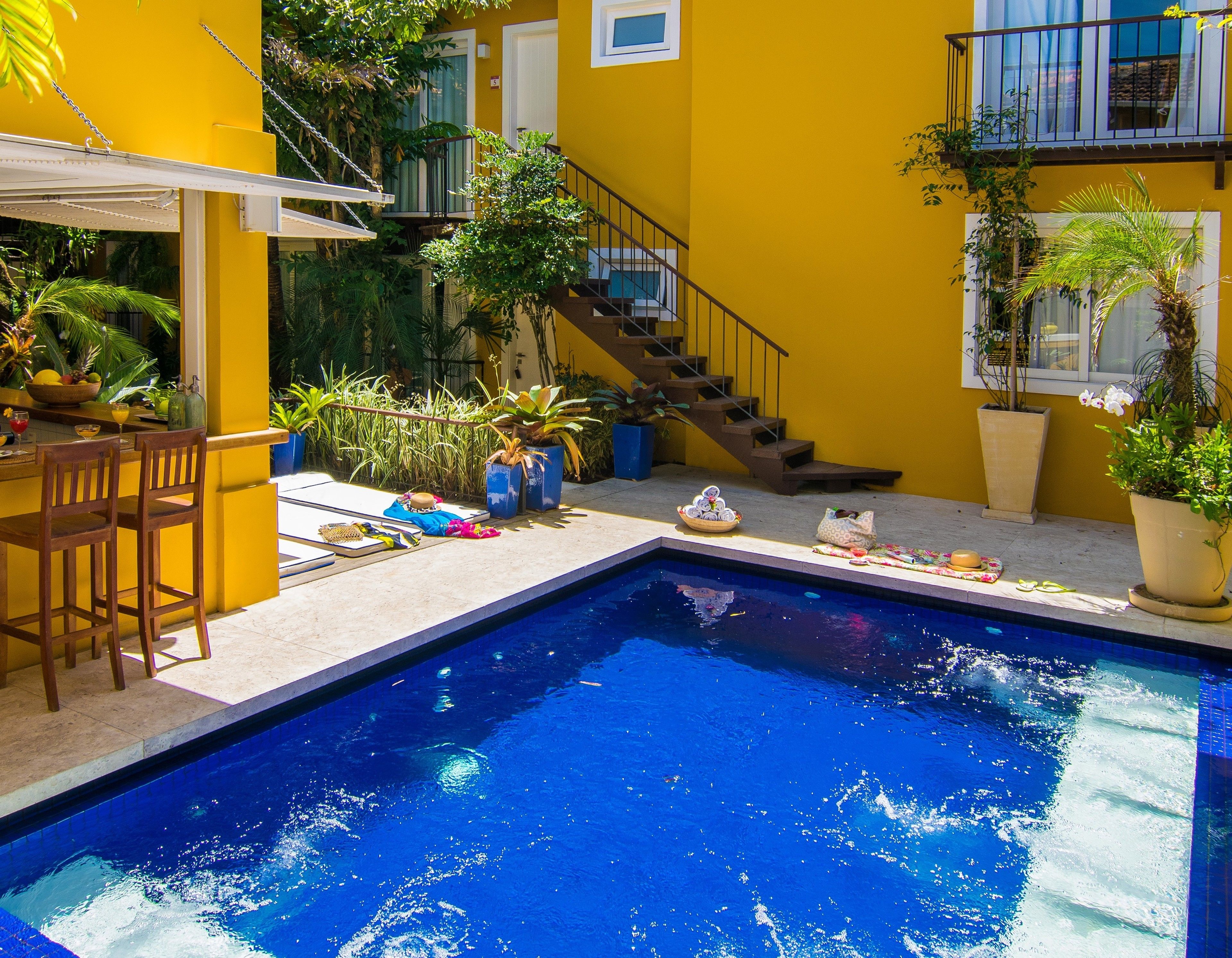 Una piscina con una escalera que conduce a un balcón, rodeada de plantas en macetas y mobiliario de exterior.