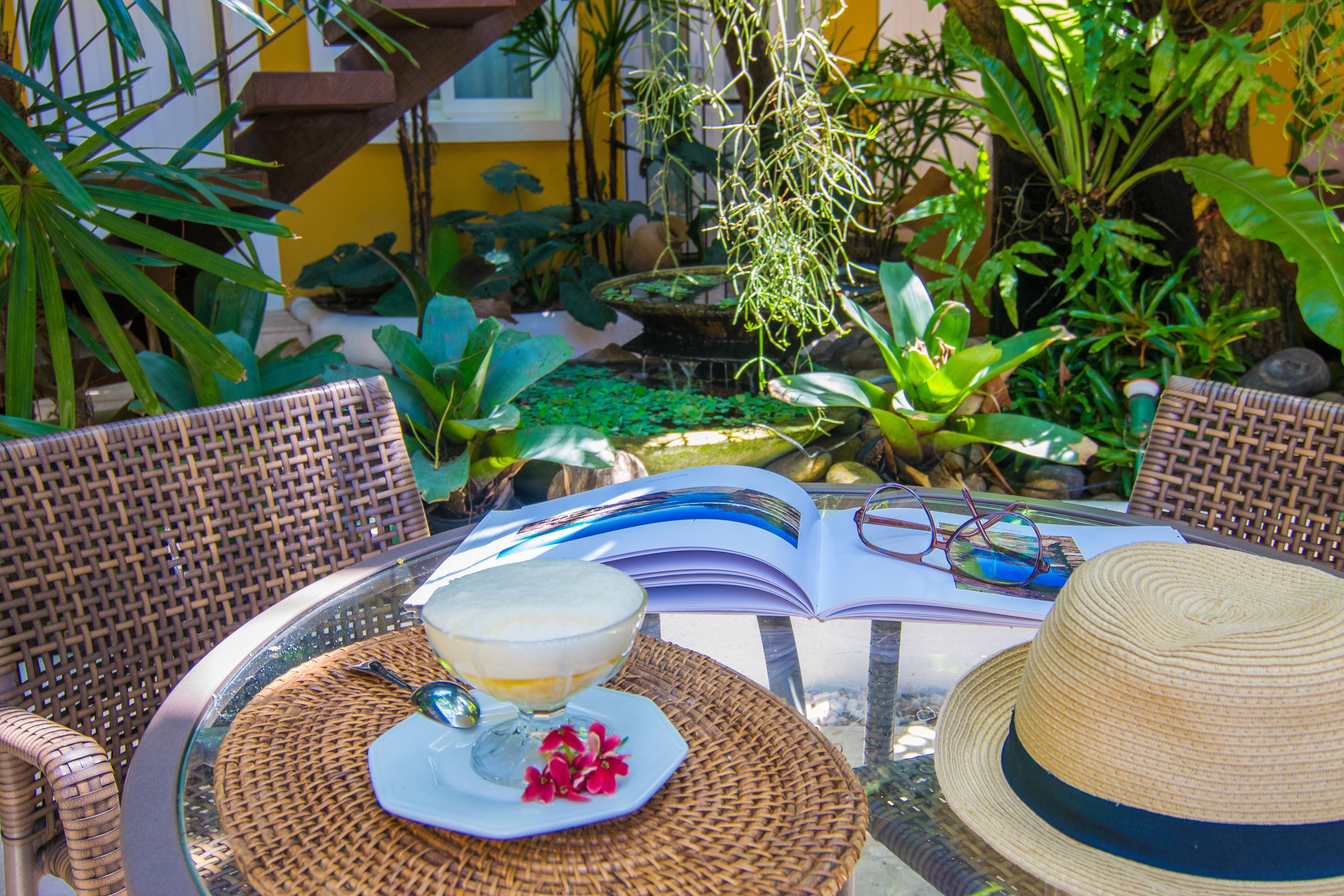 A wicker table with a glass of drink, a hat, and an open book.