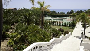 A staircase leading down to a tennis court surrounded by palm trees and greenery. - iH Hotels Agrigento Kaos Resort (Agrigento)