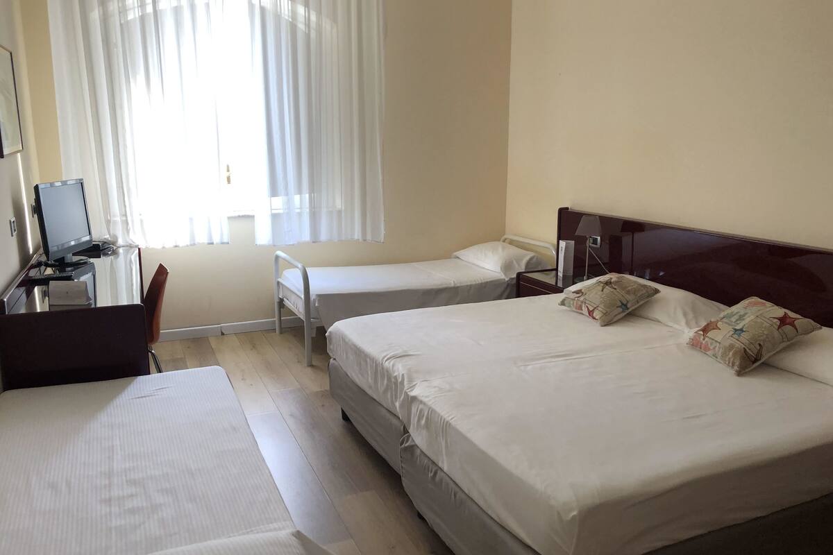 A hotel room with two beds, a desk with a computer, and a window with curtains.