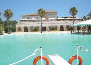 A large swimming pool with a building in the background. - iH Hotels Agrigento Kaos Resort (Agrigento)