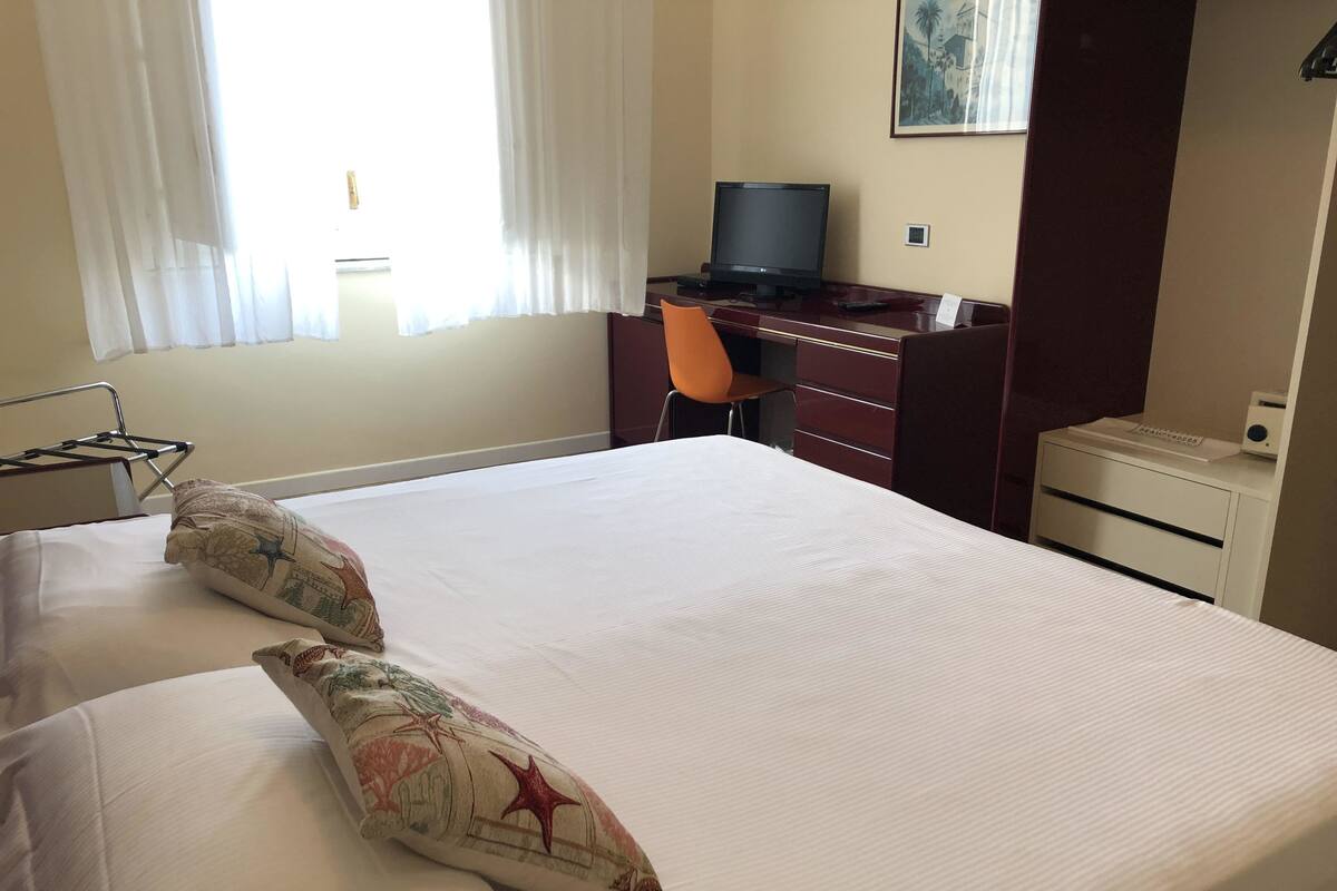 A hotel room with a bed, a desk, a chair, and a television.