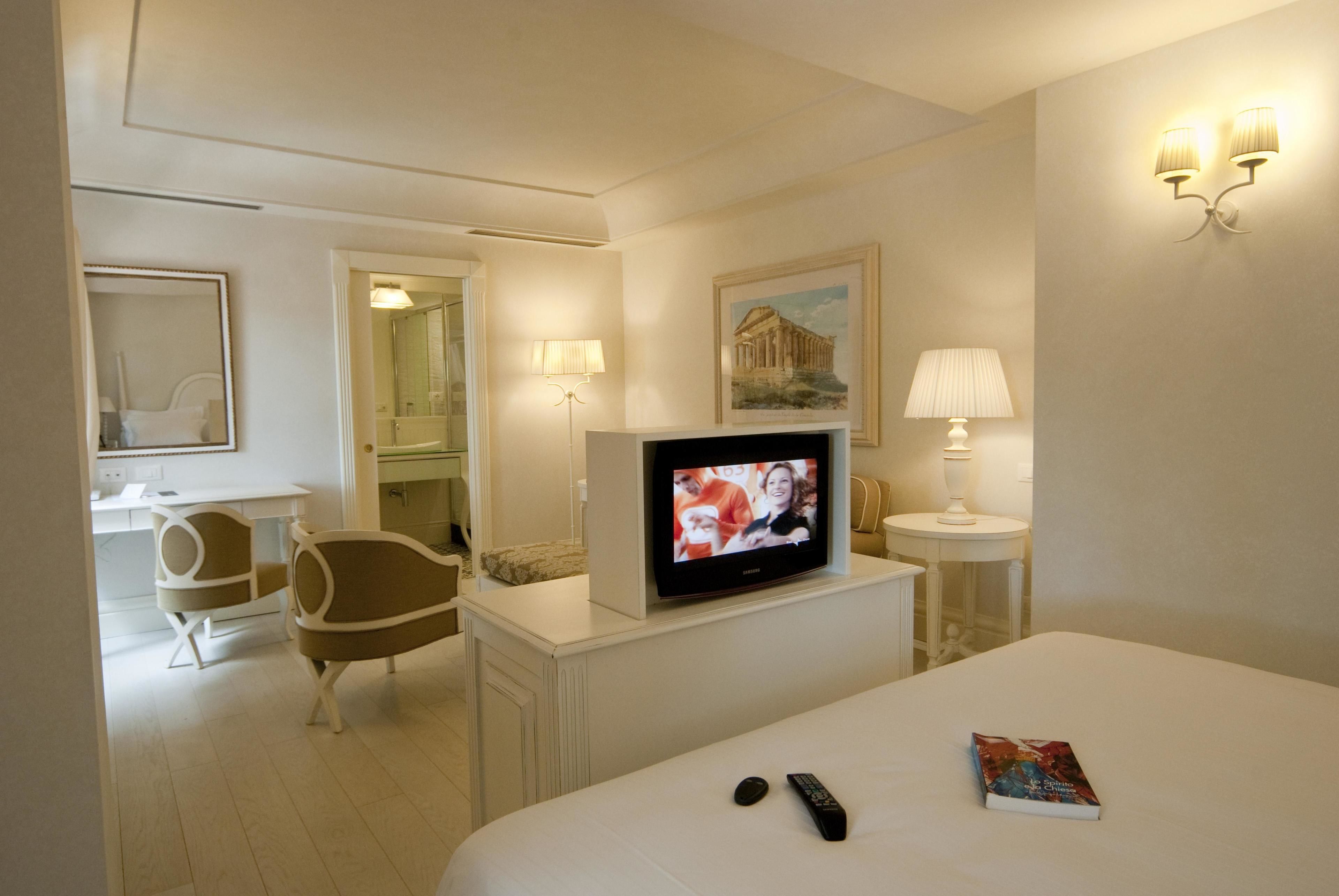 Hotellihuone, jossa on sänky, televisio, työpöytä, tuoli ja lamppu.