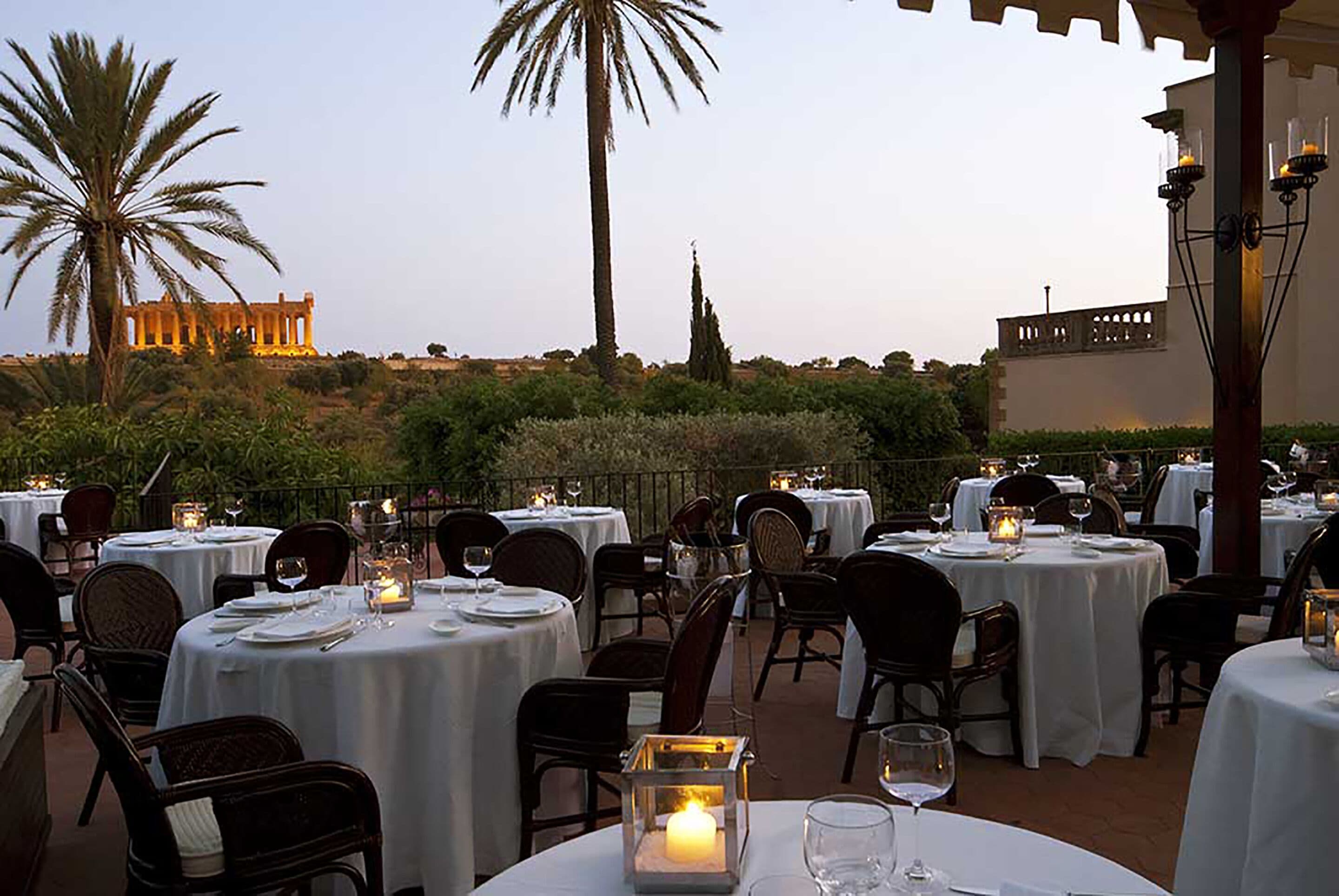 An outdoor dining area with round tables set for two, each with a candle in a lantern.