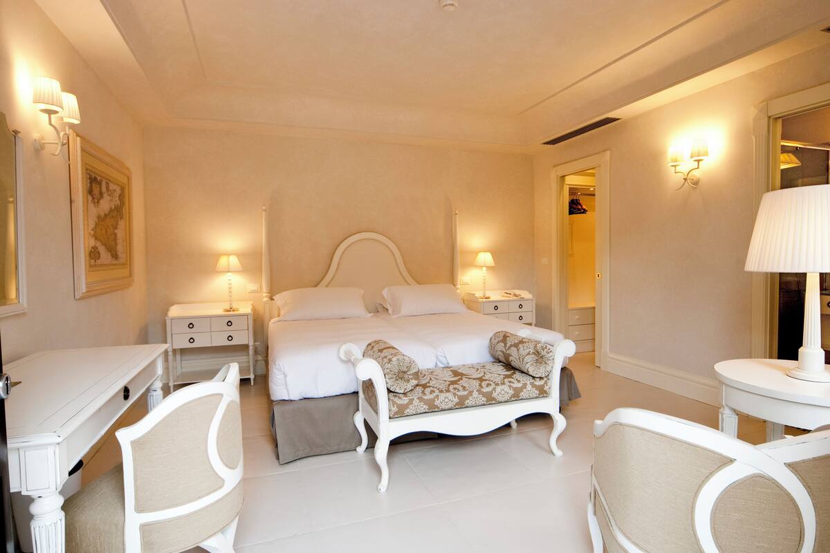 A bedroom with a large bed, bedside tables, a chair, and a desk.