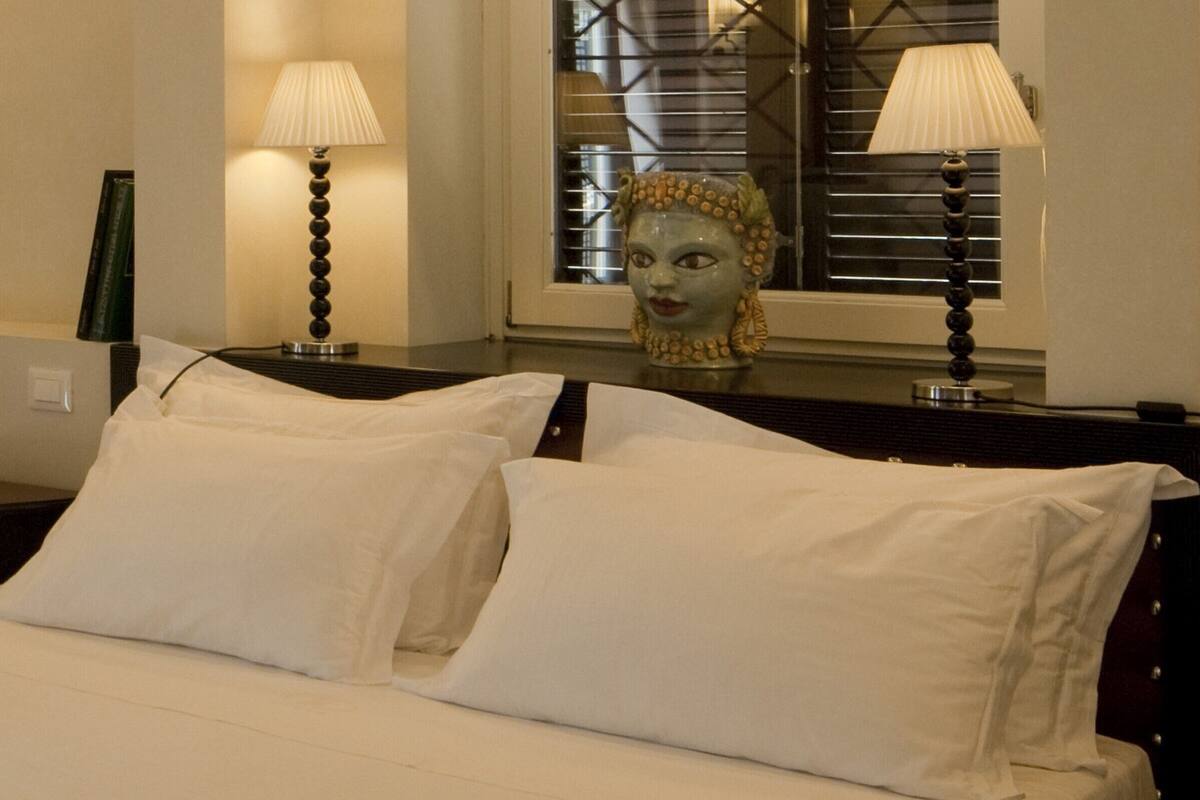 A hotel room with a bed, two lamps, and a decorative bust on the nightstand.