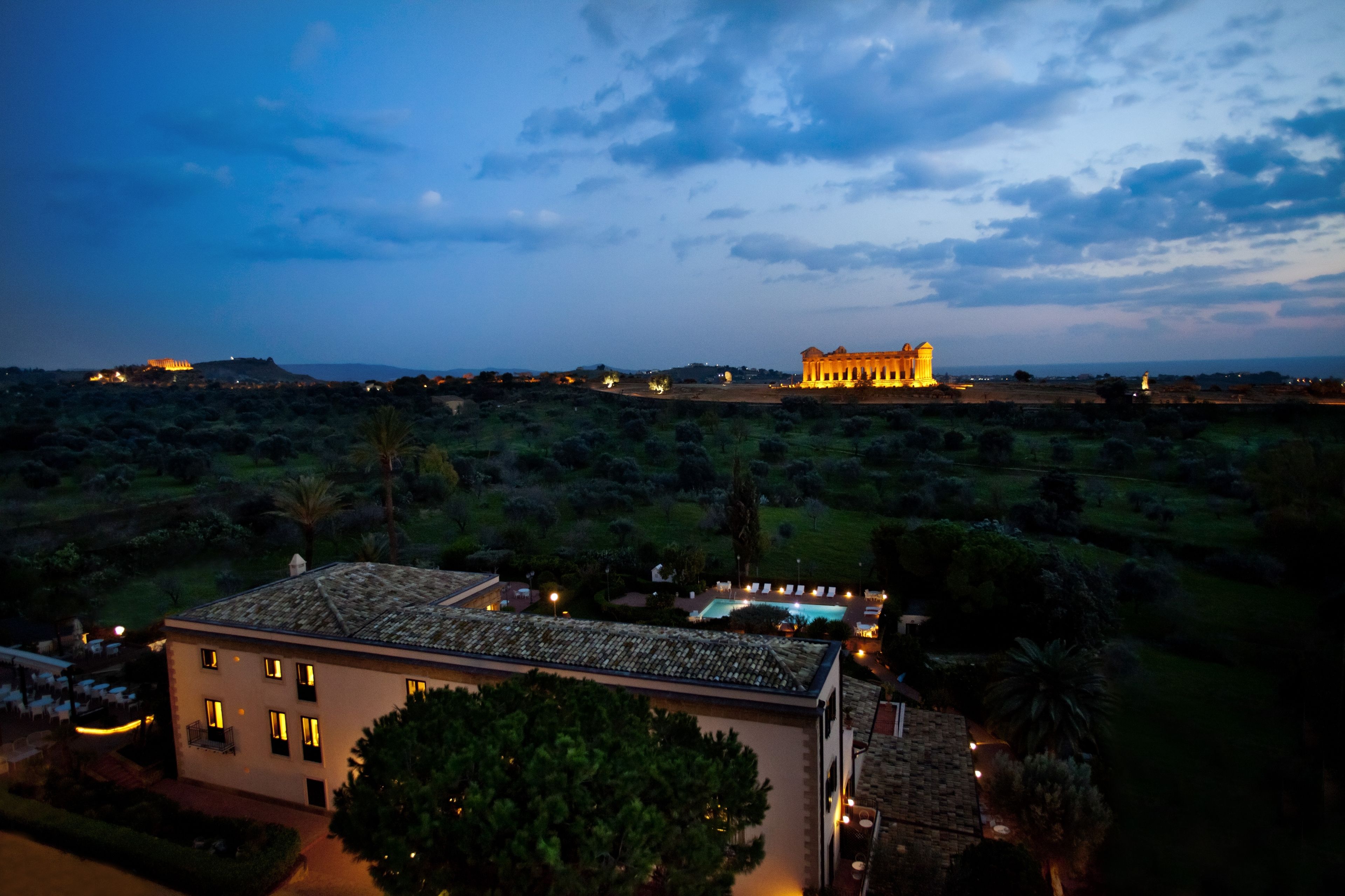 A large, illuminated building with a prominent central structure and smaller surrounding buildings, set against a backdrop of a vast, open landscape with sparse vegetation.