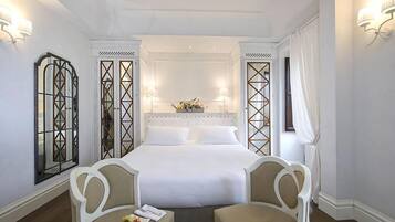Camera d'albergo con un letto grande, due sedie, un tavolino e uno specchio.