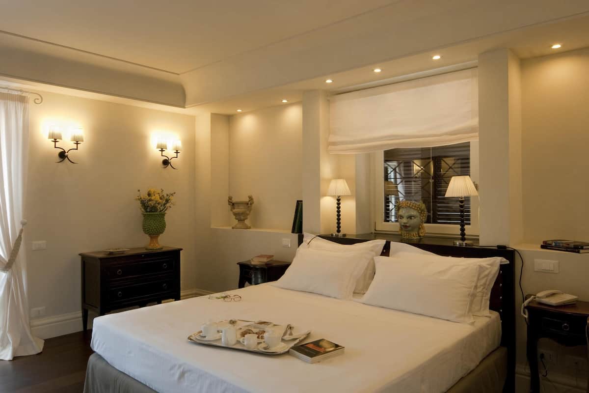 A neatly arranged hotel room with a large bed, bedside tables, a lamp, and a window with blinds.