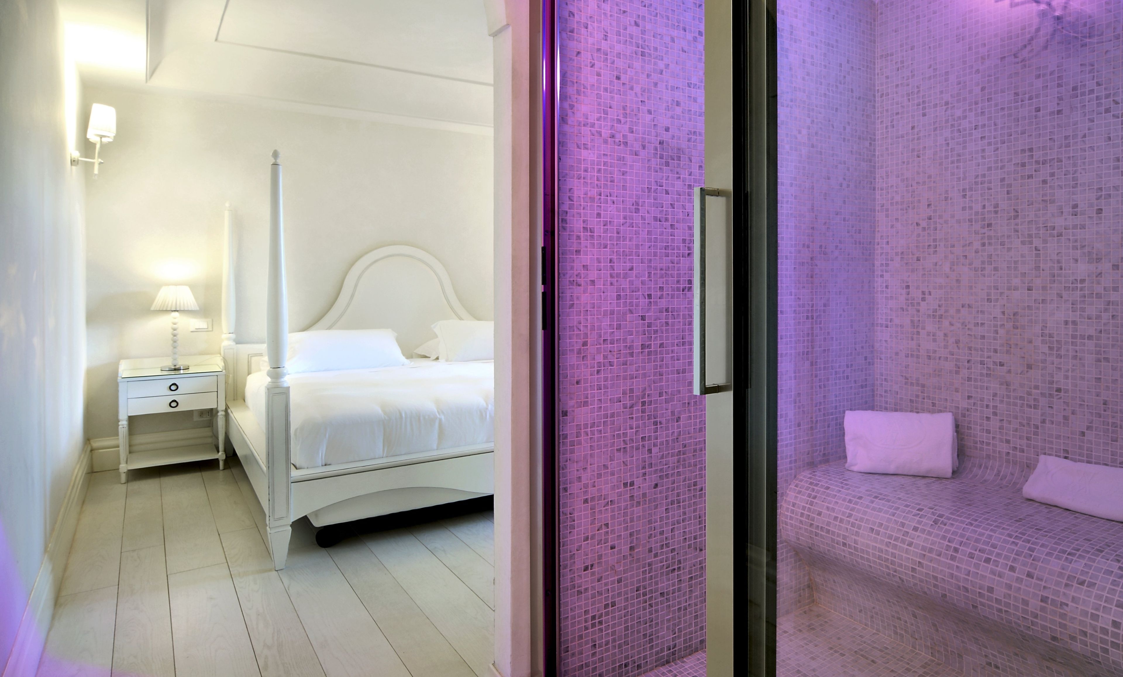 A hotel room with a bed, a nightstand, and a bathroom with a tiled shower.