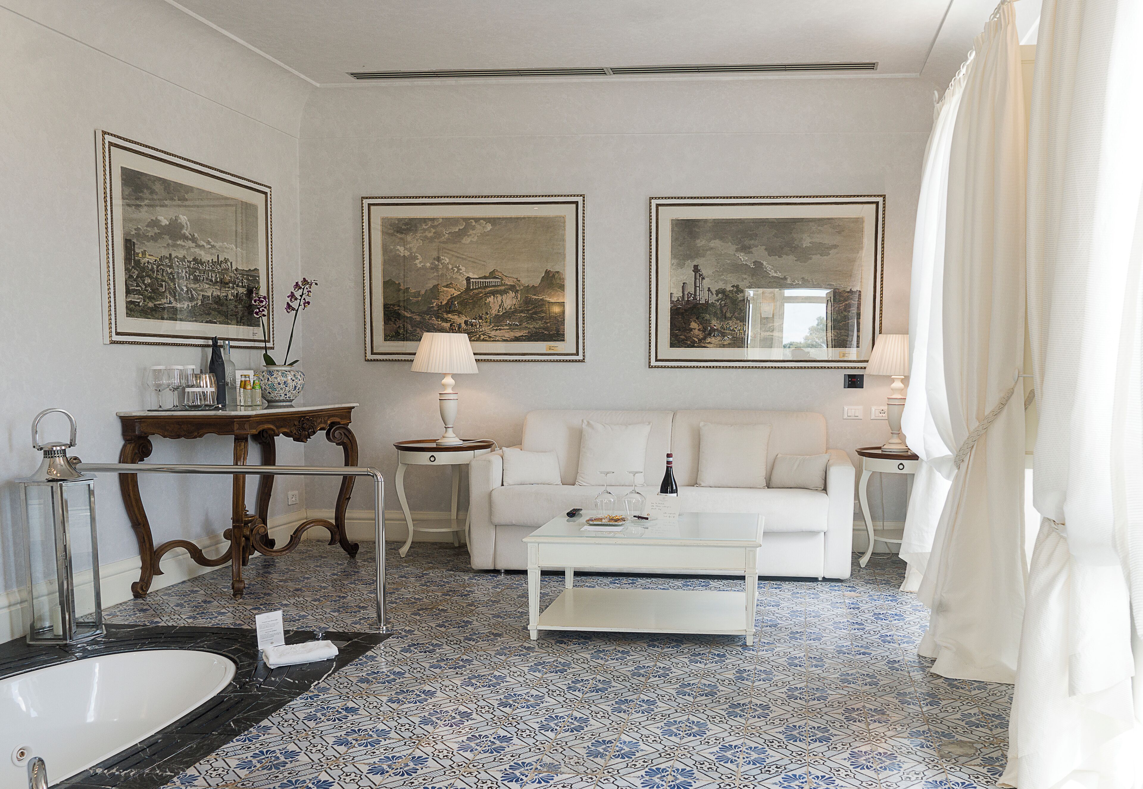 Habitación de hotel con sofá blanco, una mesita de centro, una bañera blanca y tres cuadros en la pared.