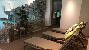 A poolside area with lounge chairs and a rock wall. - Hotel Jagdhof Glashütte (Bad Laasphe)
