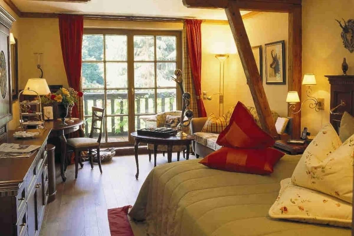 Een gezellige slaapkamer met een bed, een bureau en een stoel. Er is een raam met gordijnen en uitzicht op groen.