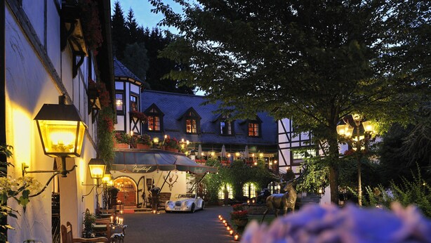 A traditional European building with a courtyard, outdoor seating, and a car parked in front. - Hotel Jagdhof Glashütte (Bad Laasphe)
