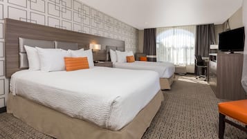 Habitación de hotel con dos camas, un escritorio, una silla, un televisor y un ventanal con cortinas.