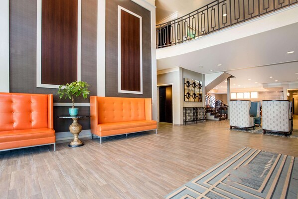 A spacious lobby with a high ceiling, a staircase, and a seating area with orange sofas.