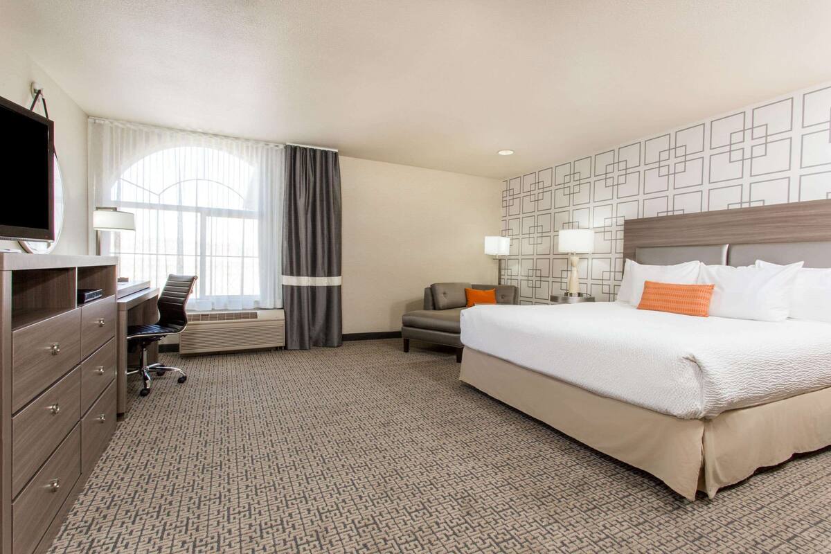 A hotel room with a large bed, a desk with a chair, a television, and a window with curtains.