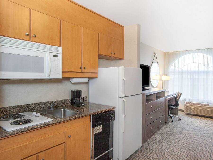 A compact hotel kitchen with wooden cabinets, a microwave, a refrigerator, a coffee maker, and a sink.
