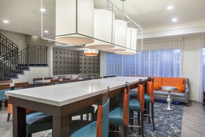 A hotel dining area with a long table, chairs, a sofa, and a staircase. - Hawthorn Suites by Wyndham Livermore Wine Country (Livermore)
