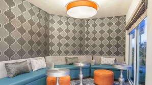 A modern lounge area with a blue sofa, orange ottomans, and patterned wallpaper. - Hawthorn Suites by Wyndham Livermore Wine Country (Livermore)