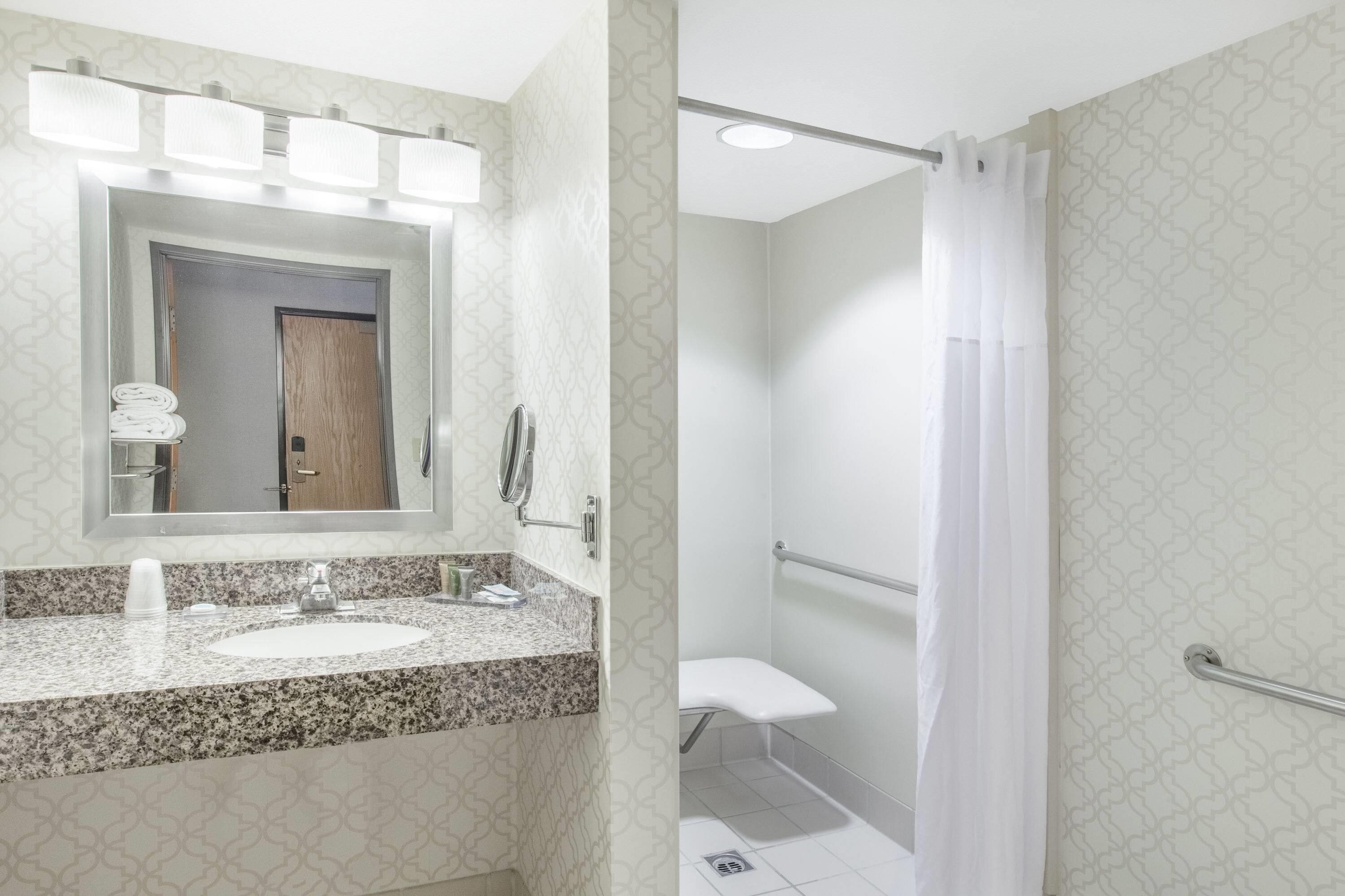 A bathroom with a granite countertop, a sink, a mirror, and a shower area with a curtain.