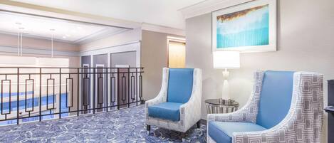 Un hall d’hôtel avec deux fauteuils à motifs, une moquette à motifs, une œuvre d’art encadrée et une vue sur l’espace du hall.
