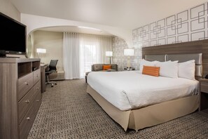 A hotel room with a large bed, a desk with a chair, a television, and a patterned wall. - Hawthorn Suites by Wyndham Livermore Wine Country (Livermore)