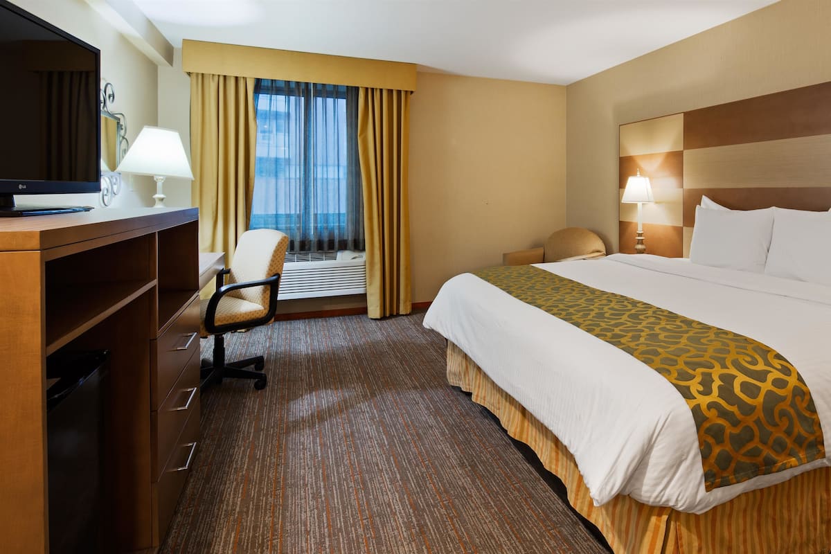 Habitación de hotel con una cama, un escritorio con ordenador, una silla, una ventana con cortinas y un equipo de aire acondicionado.