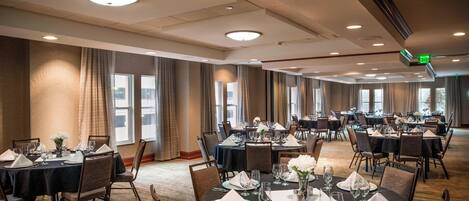 A large banquet hall with multiple round tables set for dining, equipped with chairs, tablecloths, and basic table settings.