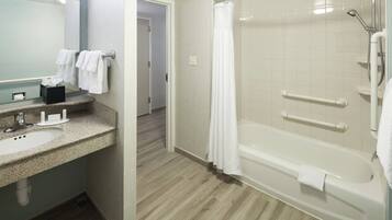 A bathroom with a sink, mirror, and a walk-in shower with grab bars.