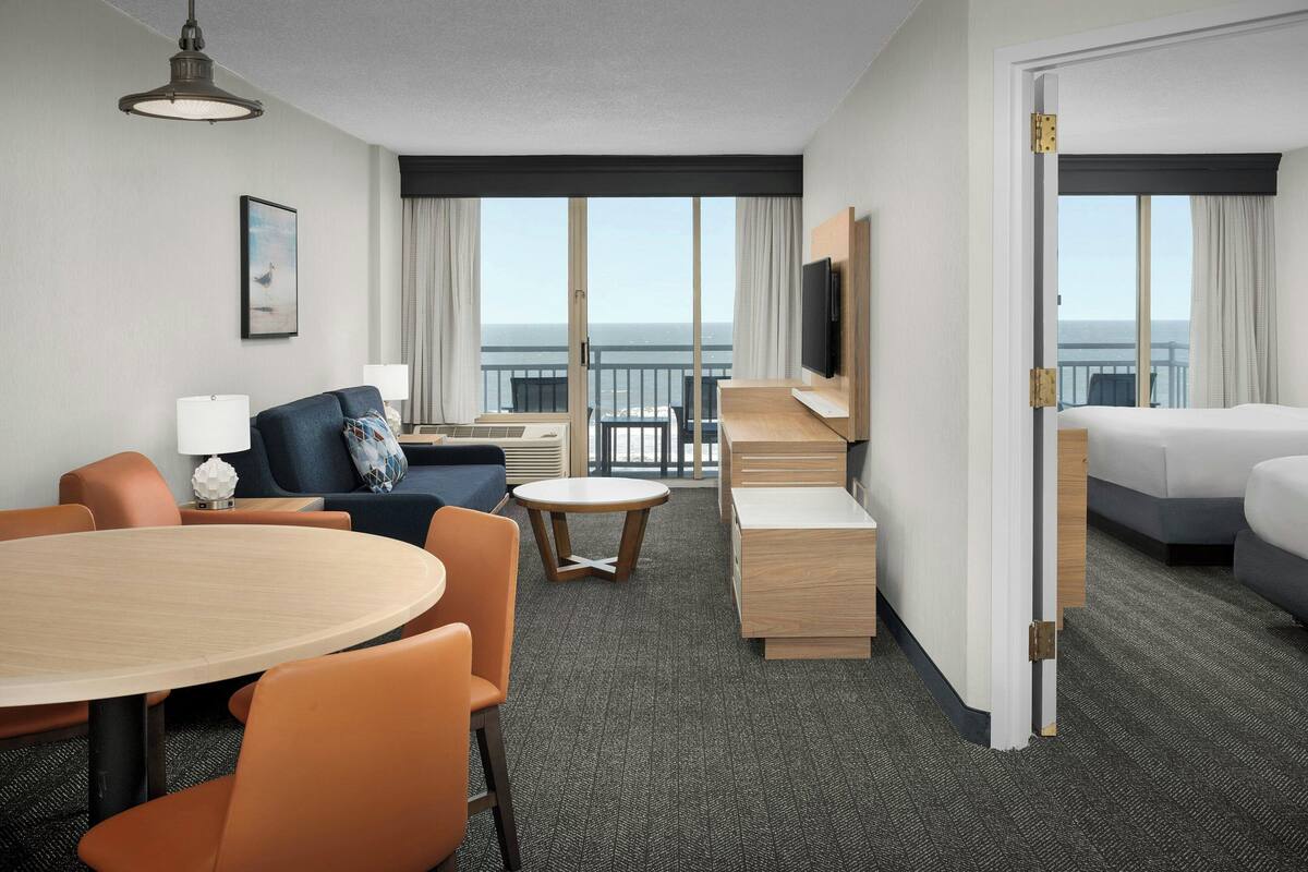 A hotel room with a balcony, a dining area, a sofa, a TV, and a bed.