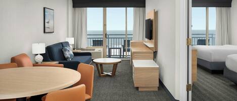 A hotel room with a balcony, a dining area, a sofa, a TV, and a bed.