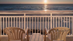 Un balcon avec deux chaises en plastique blanches, donnant sur l’océan au coucher du soleil.