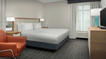A hotel room with a large bed, a desk, a chair, a TV, and a window with curtains.