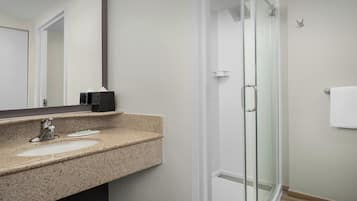 A modern bathroom with a granite countertop, a glass shower enclosure, and a white towel hanging on the wall.