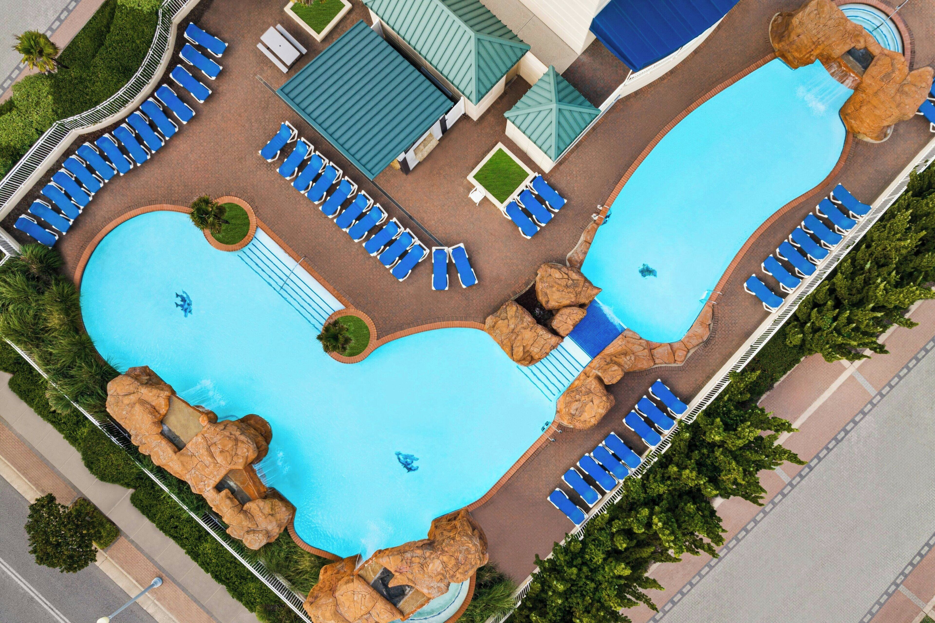 An aerial view of a hotel with two swimming pools, lounge areas, and a covered patio.