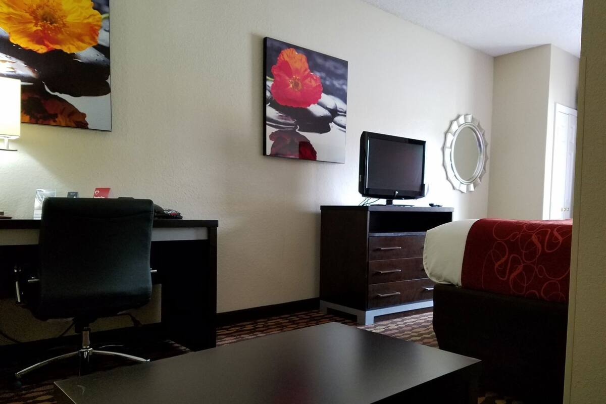 A hotel room with a desk, chair, television, and a bed with a red blanket.