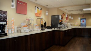 Zona de buffet con una estación de café, un refrigerador y diversos alimentos exhibidos en la barra.