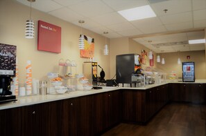 Zona de buffet con una estación de café, un refrigerador y diversos alimentos exhibidos en la barra.