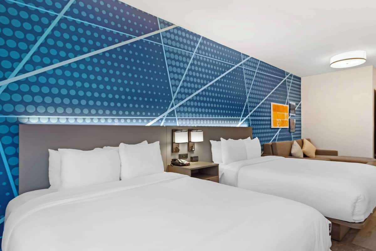 A hotel room with two beds, a nightstand with a lamp, and a wall with a geometric pattern.