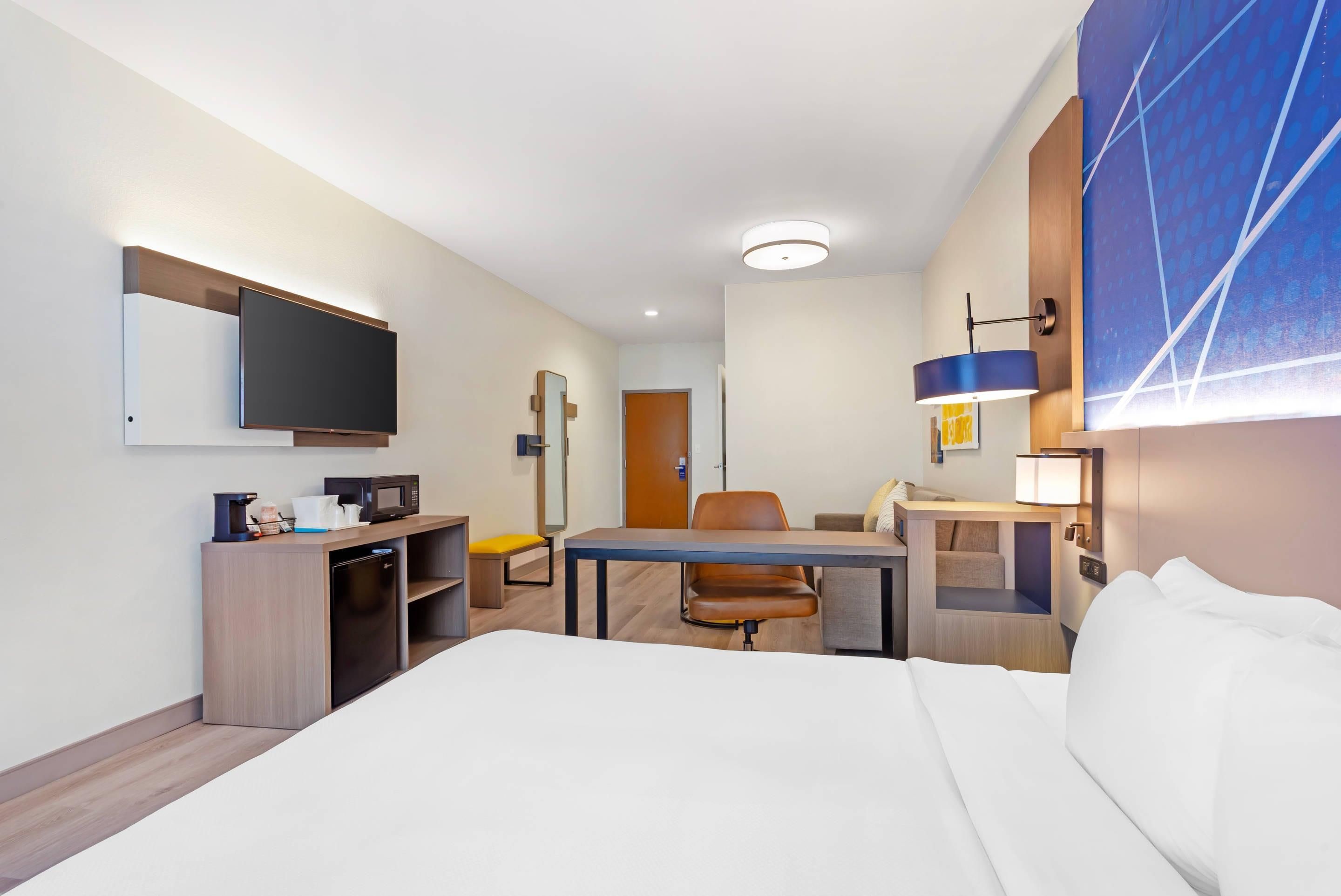A hotel room with a bed, a desk, a chair, a television, a microwave, and a small refrigerator.