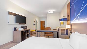 A hotel room with a bed, a desk, a chair, a television, a microwave, and a small refrigerator.